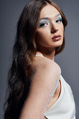 A young woman shines in a white dress, showcasing unique eye makeup amidst swirling snowflakes.