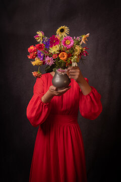 abstract renaissance portrait of anonymous girl in red dress holding a small vase with colorful dahlia flowers hiding her face