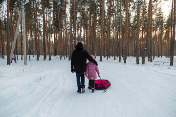 Dad with his daughter walking with snow tubing in the winter forest