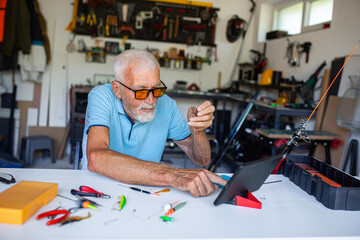 Elderly fisherman watching instructions on a tablet to set up his fishing gear