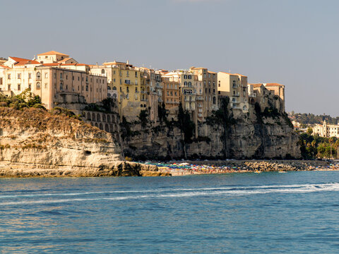Scenic view of Tropea coastline with yellow sandy beach and old town above. Blue sky, sunny day, turquoise sea with waves, colorful old buildings on the yellow rock. Summertime and leisure vibe. 