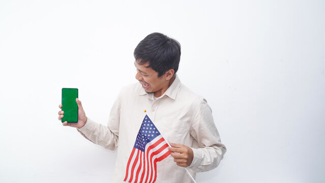Asian Man holding green screen smartphone with USA flag at studio against white background - Powered by Adobe