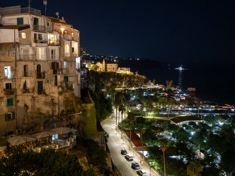 Tropea old town and coast at night. House building on the left, street bellow and sea at the right. Artificial night lights and city illumination.