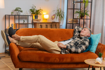 Tired young man with gray hair sitting on comfortable couch, taking a rest, daytime nap. Portrait...