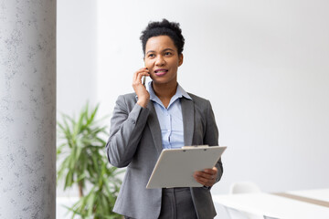 Professional female executive communicating via smartphone, managing paperwork while multitasking in contemporary corporate workspace