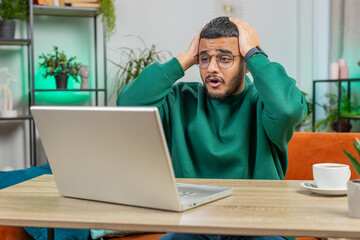 Displeased sad Indian man use laptop notebook typing browsing working, loses becoming surprised...