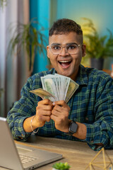 Rich pleased happy Indian man waving money dollar cash banknotes bills like a fan success business...