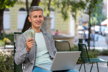 Happy rich man using laptop winner victory counting holding fan of cash money in dollar banknotes...