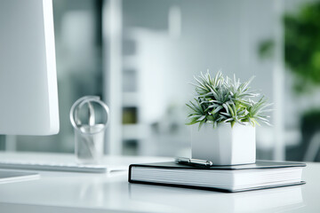 Minimalist office desk with a small potted plant, a closed notebook, and a pen, set against a blurred background featuring a computer monitor and modern decor
