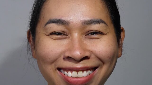 A close-up portrait of an Asian woman smiling happily, showing teeth and facial wrinkles around the eyes.