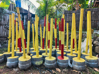 Collection of handmade yellow and red painted bamboo poles set in concrete bases for a traditional...