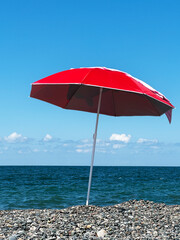 Red umbrella placed on sea pebbles against the sea background