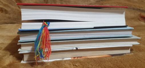 A colorful rainbow tassel bookmark marks a page in a stack of books. A powerful symbol of reading,...