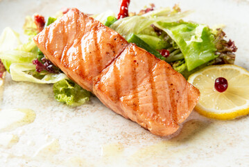 Grilled salmon fillet with glaze, served on mixed leafy greens, garnished with red berries and lemon slice. Elegant, healthy meal presentation