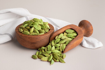 Whole green cardamom spice aromatic pods in wooden bowl and scoop. Green cardamom spice. 