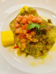 Breaded fillet of plaice served with fresh cherry tomatoes and sliced onions on a white plate