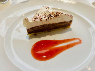 Slice of layered chocolate and cream cake served on a white plate with a decorative smear of bright...