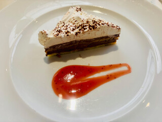 Slice of layered chocolate and cream cake served on a white plate with a decorative smear of bright...