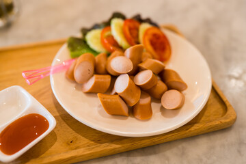 Slice pork sausages served with slice tomato and sliced cucumber and chili sauce on wood tray