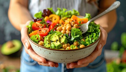 Close-up of a woman in jeans and a sweater holding a bowl of vegan salad with avocado, grains, beans, and roasted vegetables. Healthy eating and plant-based diet.