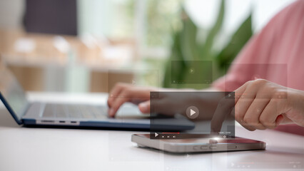 Hands using smartphone and laptop with video play icons, concept of video streaming, digital content creation, online media marketing, and modern communication technology.