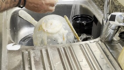 Close-up of man washing dishes at home in the kitchen, male hands cleaning plate with sponge and soap under running water at sink, domestic chores, household cleaning, everyday lifestyle scene - Powered by Adobe