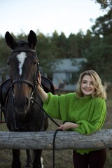 A young woman with blonde hair smiles joyfully while interacting with a dark horse, set against a...