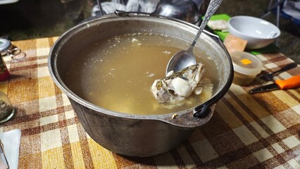 On the table covered with an oilcloth tablecloth stands a cast-iron cauldron with pike soup cooked over a fire. The fish was caught while fishing on the river