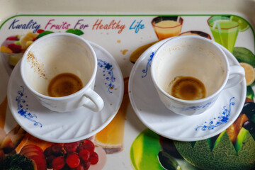 Close-up of two empty white ceramic teacups and saucers with visible brown tea stains on a tray...
