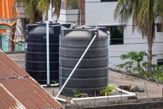 Two large black plastic water tanks sit on a residential rooftop in Bangladesh, connected by visible water pipes, showcasing an essential element of urban infrastructure.