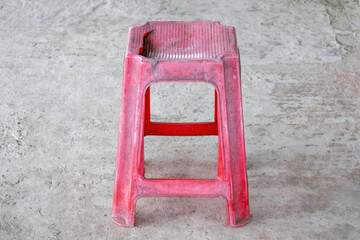 A worn-out red plastic stool rests on a concrete ground.