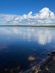 The shore of a lake with reflecting clouds on a sunny summer day. Vacation on the coast . Nature background