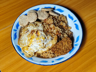Authentic Indonesian fried rice with sunny side up egg, crackers and fried tempeh on a classic enamel plate.