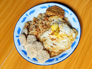 Authentic Indonesian fried rice with sunny side up egg, crackers and fried tempeh on a classic enamel plate.