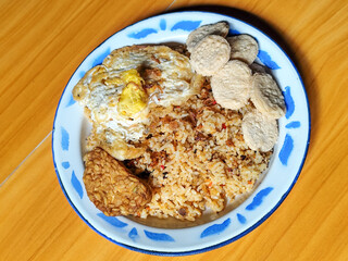 Authentic Indonesian fried rice with sunny side up egg, crackers and fried tempeh on a classic enamel plate.