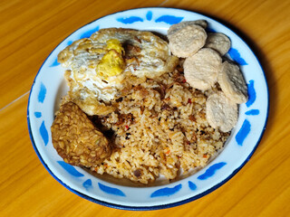 Authentic Indonesian fried rice with sunny side up egg, crackers and fried tempeh on a classic enamel plate.