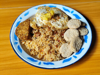 Authentic Indonesian fried rice with sunny side up egg, crackers and fried tempeh on a classic enamel plate.