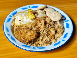 Authentic Indonesian fried rice with sunny side up egg, crackers and fried tempeh on a classic enamel plate.