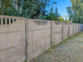 Long concrete privacy fence panels creating boundary between residential properties with trees in background. High quality photograph