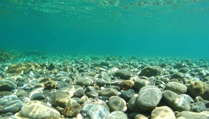 Sunlight filters through clear turquoise water, illuminating a bed of smooth, various-sized stones beneath the surface.
