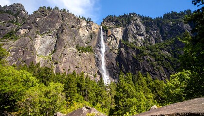 A dramatic waterfall cascades down steep granite cliffs, surrounded by lush greenery in a majestic natural landscape.