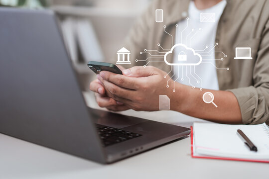Close-up of man holding smartphone in front of laptop with cloud computing icons overlay. Concept of digital technology, cybersecurity, data storage, online banking, and modern cloud solutions - Powered by Adobe
