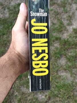 Hand Holding "The Snowman" by Jo Nesb&oslash; Book Spine