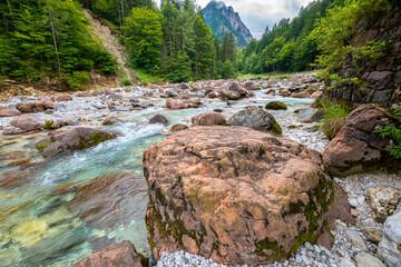 Serene view of red rocks in the turquoise colored Slizza river, south of Tarvisio in the Julian Alps, Italy