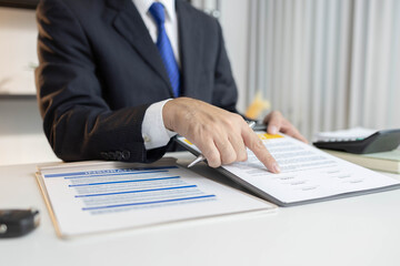 
A man in a suit is signing a contract. He is holding a pen and looking at the contract

