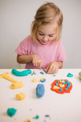 Young girl creates colorful shapes and designs with play dough in a bright room