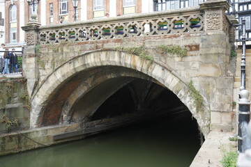 Obraz premium Lincoln, Lincolnshire, England - August 21 2025: Medieval stone bridge over river with historic architecture.