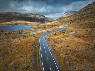 Aerial drone view of wet winding road in the Swiss Alps, Switzerland, with alpine lake, dramatic...