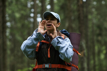 Young adult Caucasian woman standing in forest calling out with hands around mouth, wearing...