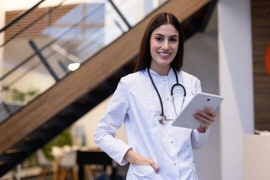 Professional female physician reviewing medical data on tablet while walking through bright hospital hallway, demonstrating clinical expertise
